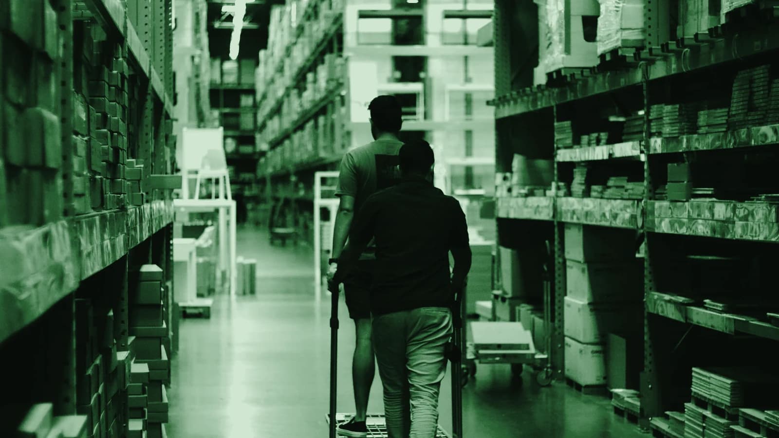 Two people walking a trolley down a wholesale warehouse aisle
